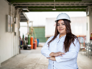Una joven salvadoreña sonríe a la cámara; lleva puesta una blusa blanca y un casco de seguridad del mismo color. Tiene los brazos cruzados.
