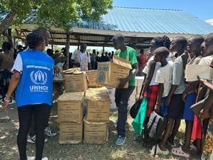 Mujeres, niñas y niños hacen fila para recibir paquetes de ayuda en cajas de cartón por parte de un miembro del personal de ACNUR