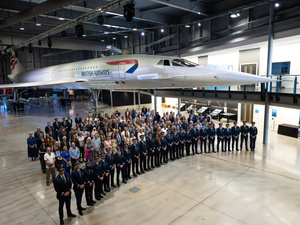 Una fila de pilotos posa delante de un grupo de personas en un hangar con un avión concorde detrás de ellos