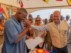 Un hombre sonriente dibuja con un lápiz un retrato del Alto Comisionado, quien le saluda calurosamente tocándole el hombro, delante de muchas personas que le acompañan.