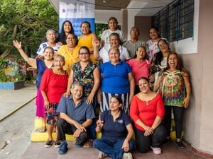 Quince mujeres adultas mayores, dos mujeres jóvenes, y un hombre adulto mayor, posan para la foto a las afueras de un aula