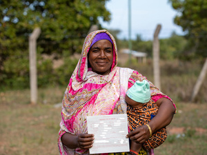 Una mujer Pemba de Kenia sonríe mientras sostiene a su bebé en brazos. Muestra orgullosa un documento