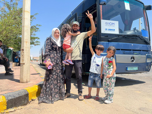 Un hombre, una mujer con sus dos niñas y un niño, posan para la foto de pie frente a un autobús de pasajeros