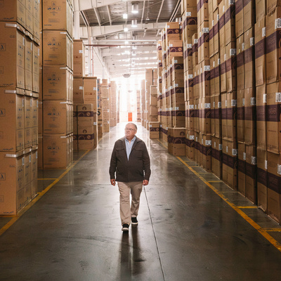 A man walks between towering stacks of cardboard boxes in a warehouse
