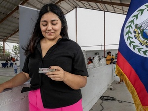 Una mujer de cabello negro, vestida de blusa negra y pantalón rosa, sostiene en su mano izquierda una tarjeta de residencia
