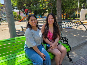 Dos mujeres jóvenes posan para la foto, de pie en un parque con árboles al fondo