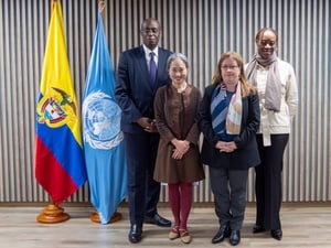 Un hombre y tres mujeres posan para una foto de grupo institucional al lado de las bandares de Colombia y de la ONU.