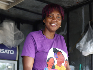 Una mujer con playera morada sonríe desde la ventana de un comedor comunitario