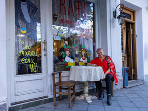 Una mujer de cabello corto que viste blusa roja y pantalón negro, sentada afuera de un restaurante.