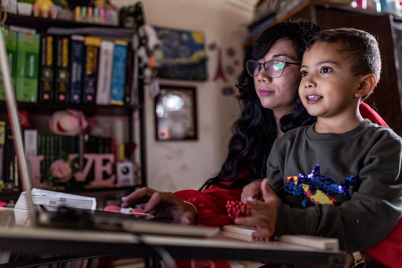Una mujer con anteojos trabaja en un computador. En su regazo, está sentado un niño que observa lo que ella hace.