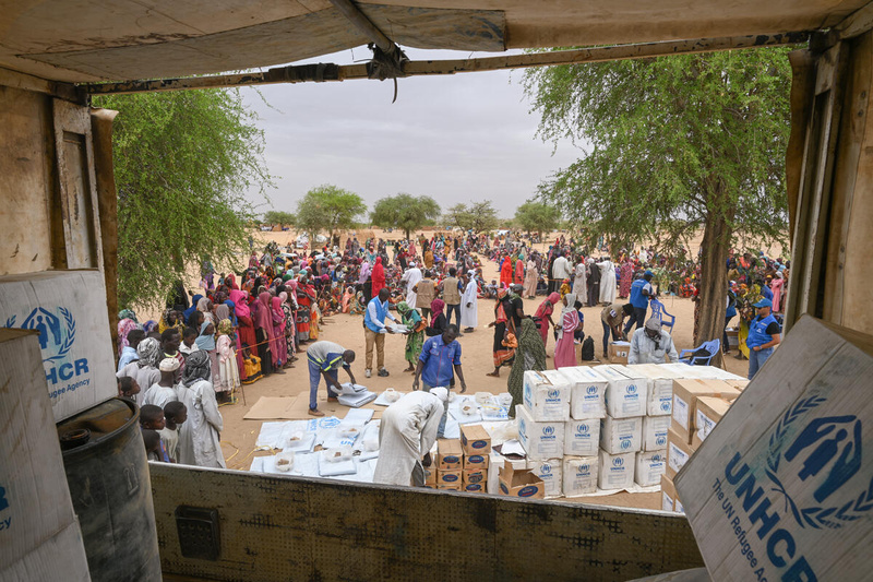Vista desde la parte trasera de un camión que muestra a personas descargando suministros de ayuda para los refugiados que esperan cerca