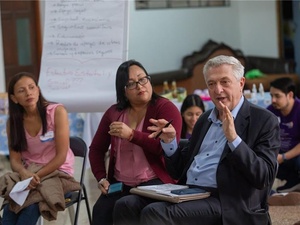 Dos mujeres y un hombre conversan sentados en un salón.