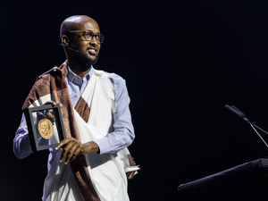 Un hombre somalí, que usa anteojos y viste un traje tradicional, sonríe mostrando la medalla que recibió por haber sido electo ganador global del Premio Nansen