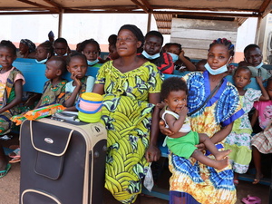 Un numeroso grupo de refugiados centroafricanos repatriados sentados en bancos con sus pertenencias, en el exterior de un alberge al aire libre